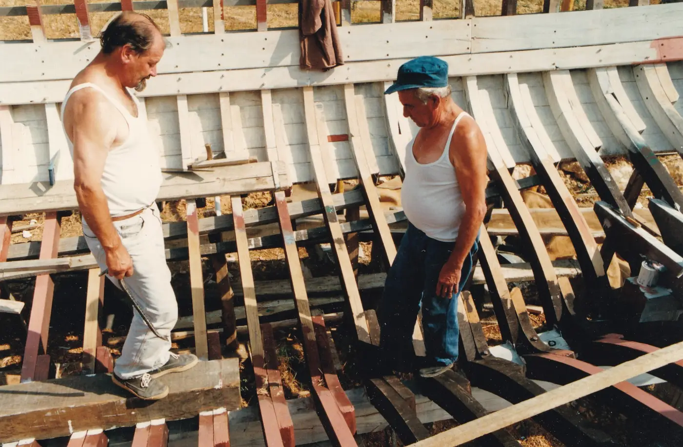 Two shipwrights working along the ribs of the hull